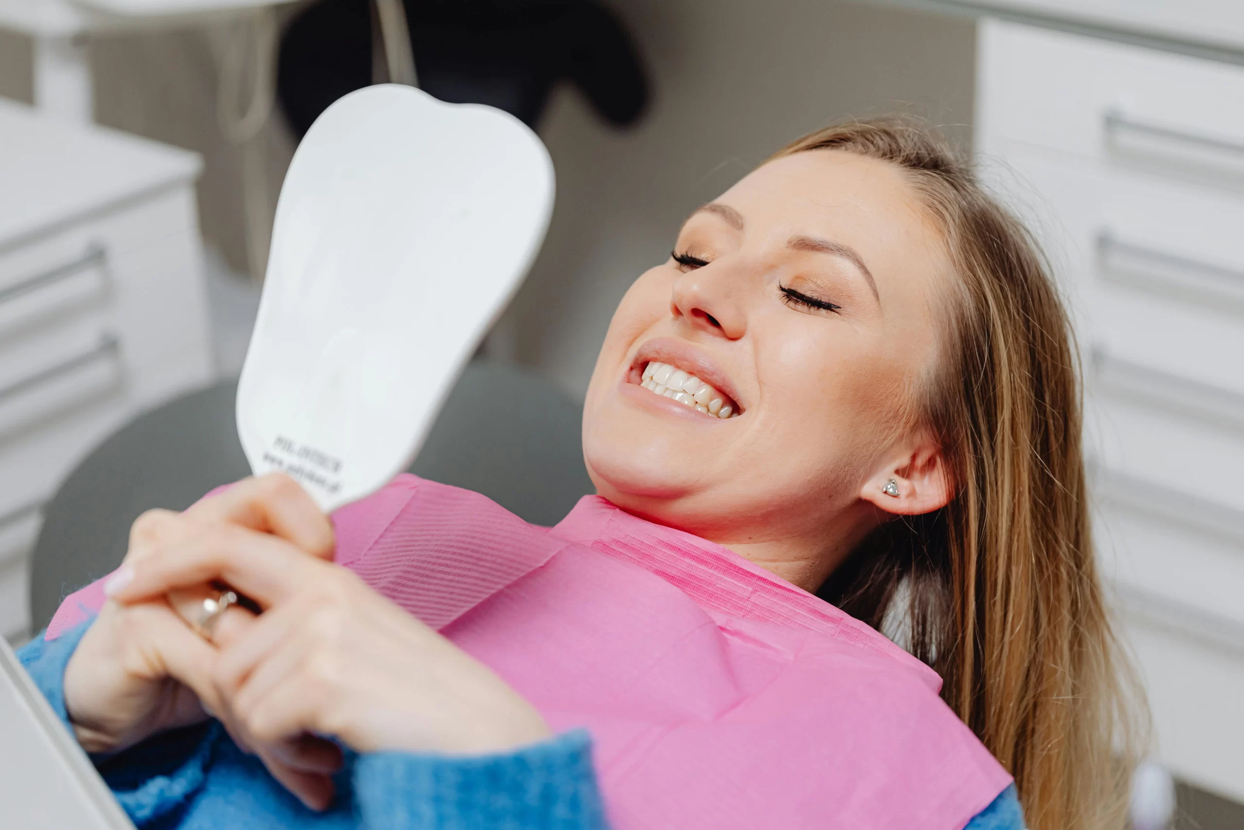 Smiling woman looking at the mirror after her teeth whitening session.
